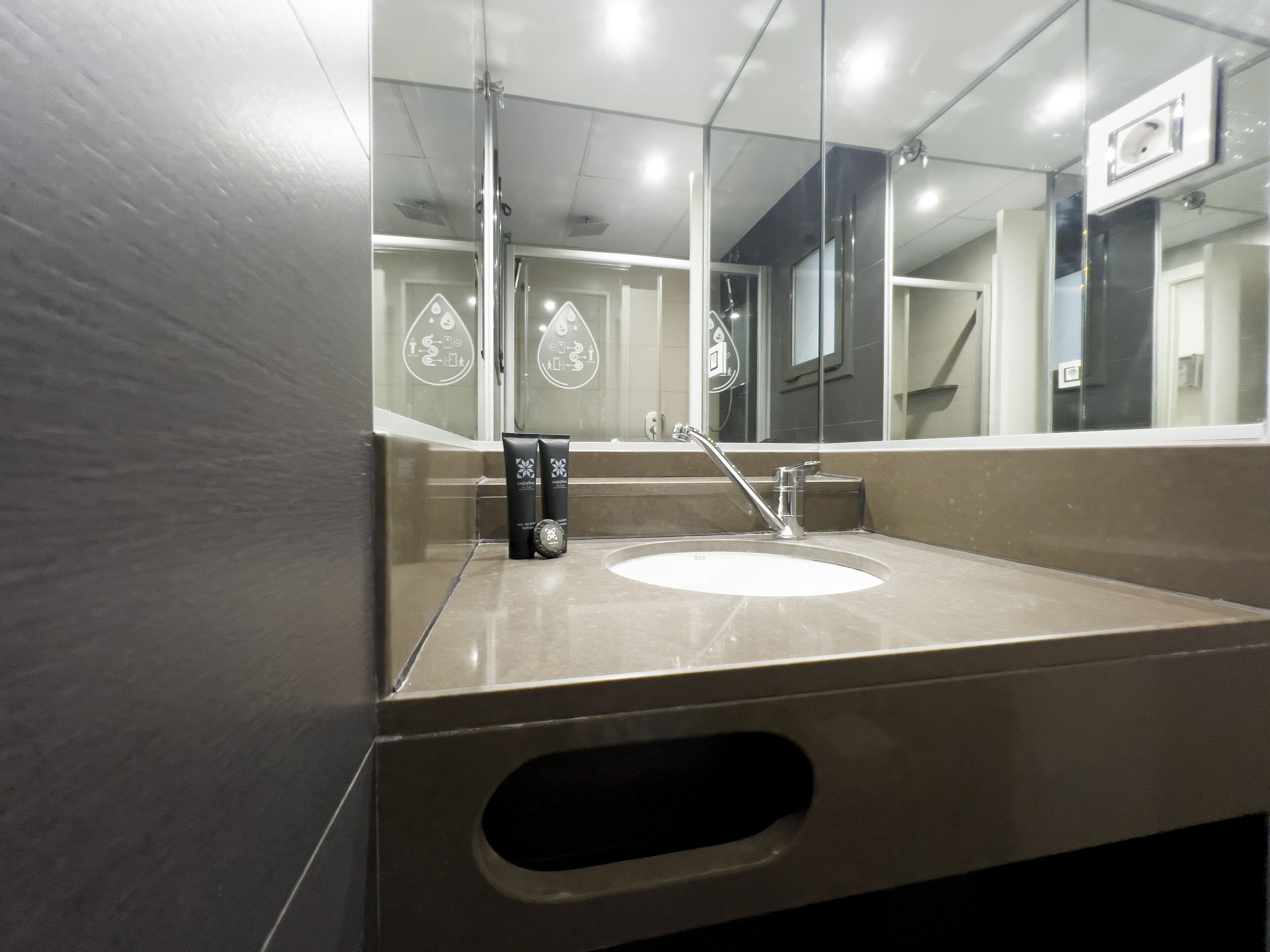 A modern bathroom with a large mirror, a sink, and two toiletries.