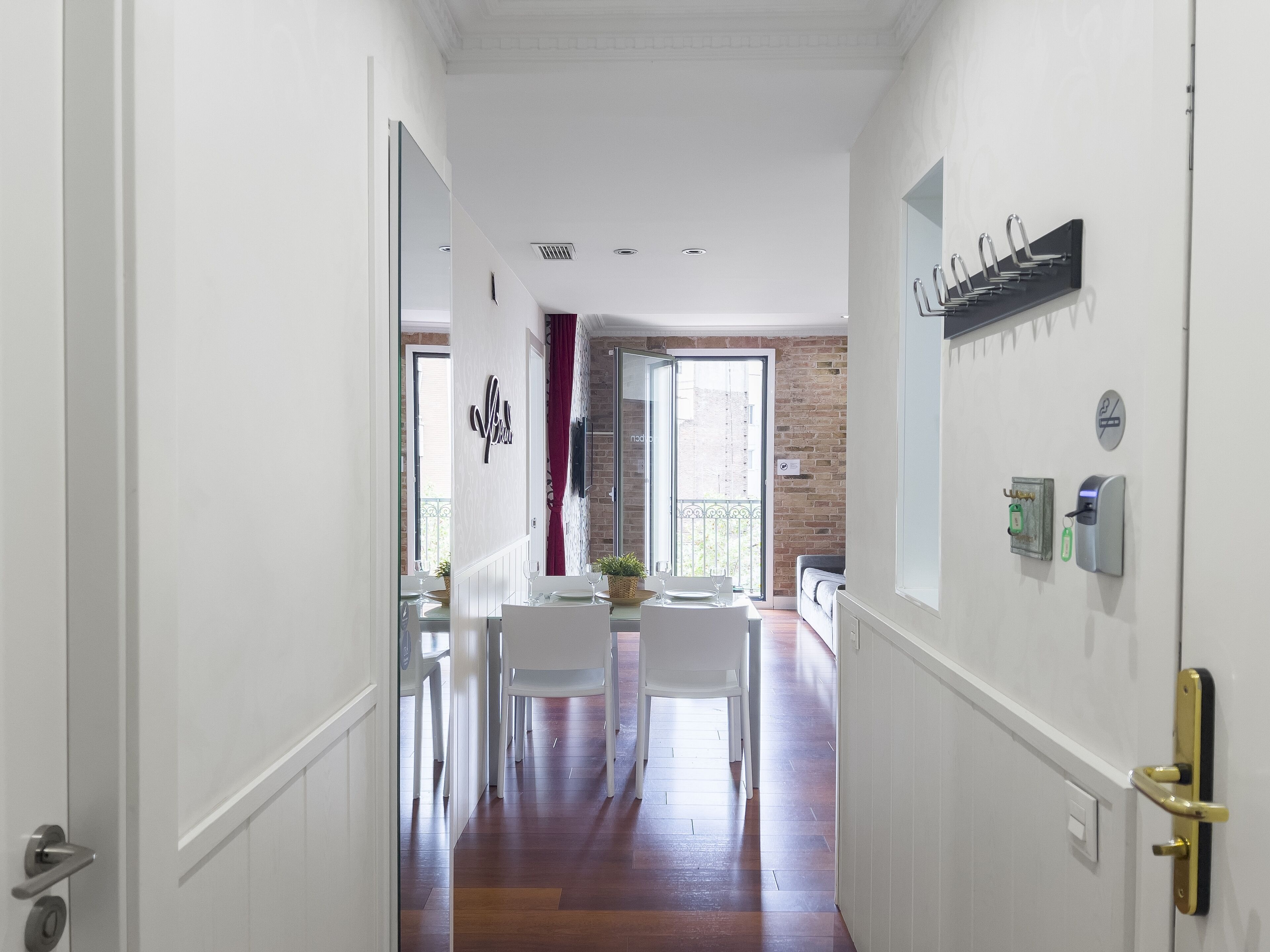 A hallway leading to a dining area with a table set for two, a door with a key lock, and a wall-mounted key holder.