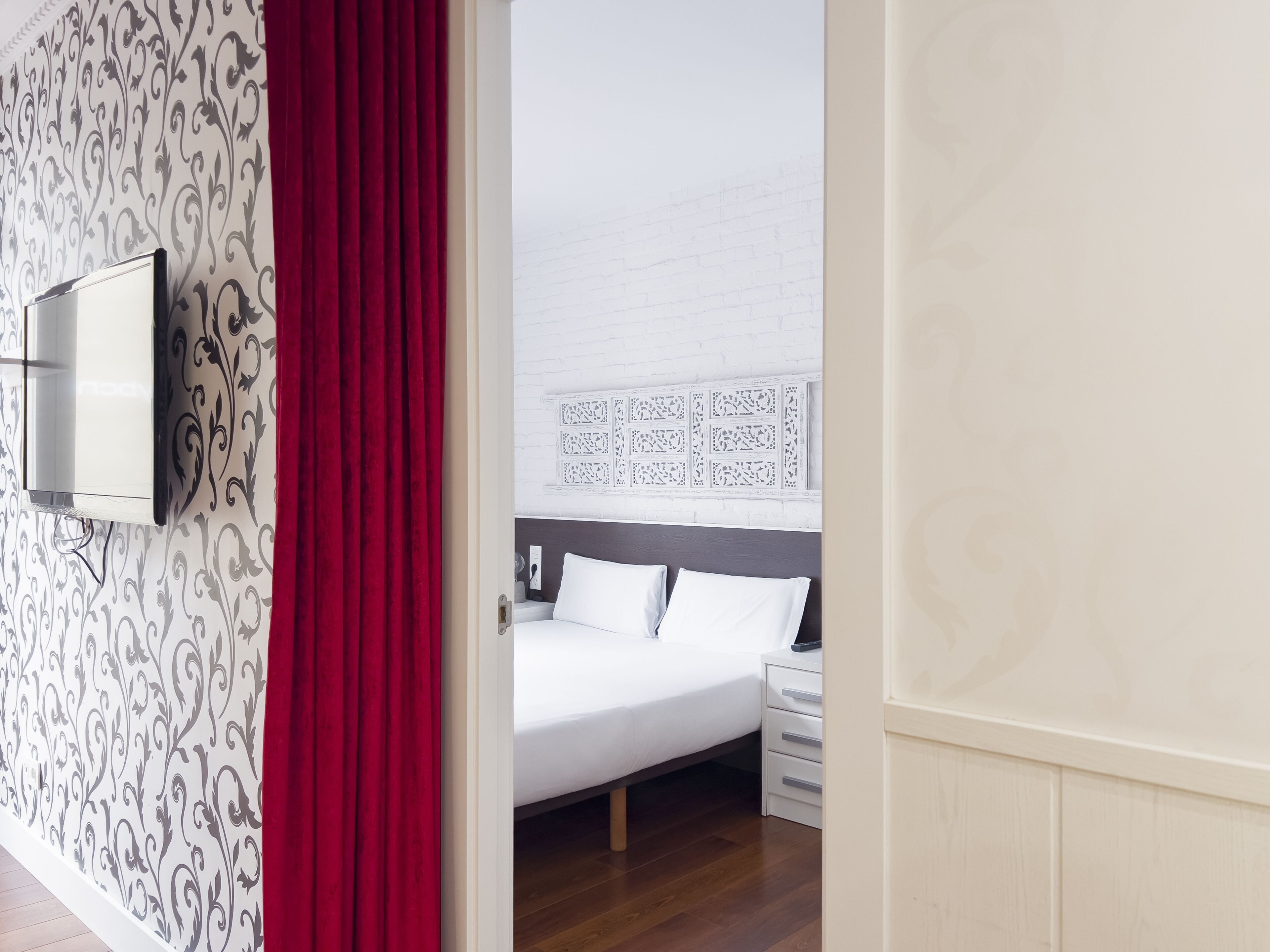 A hotel room with a bed, bedside table, and a TV mounted on the wall.