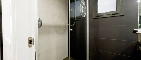 Un baño moderno con ducha de vidrio, paredes de azulejos blancos y oscuros, y un ventanal.