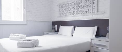 A modern bedroom with a large bed, white linens, a nightstand with a lamp, and a decorative wall panel.
