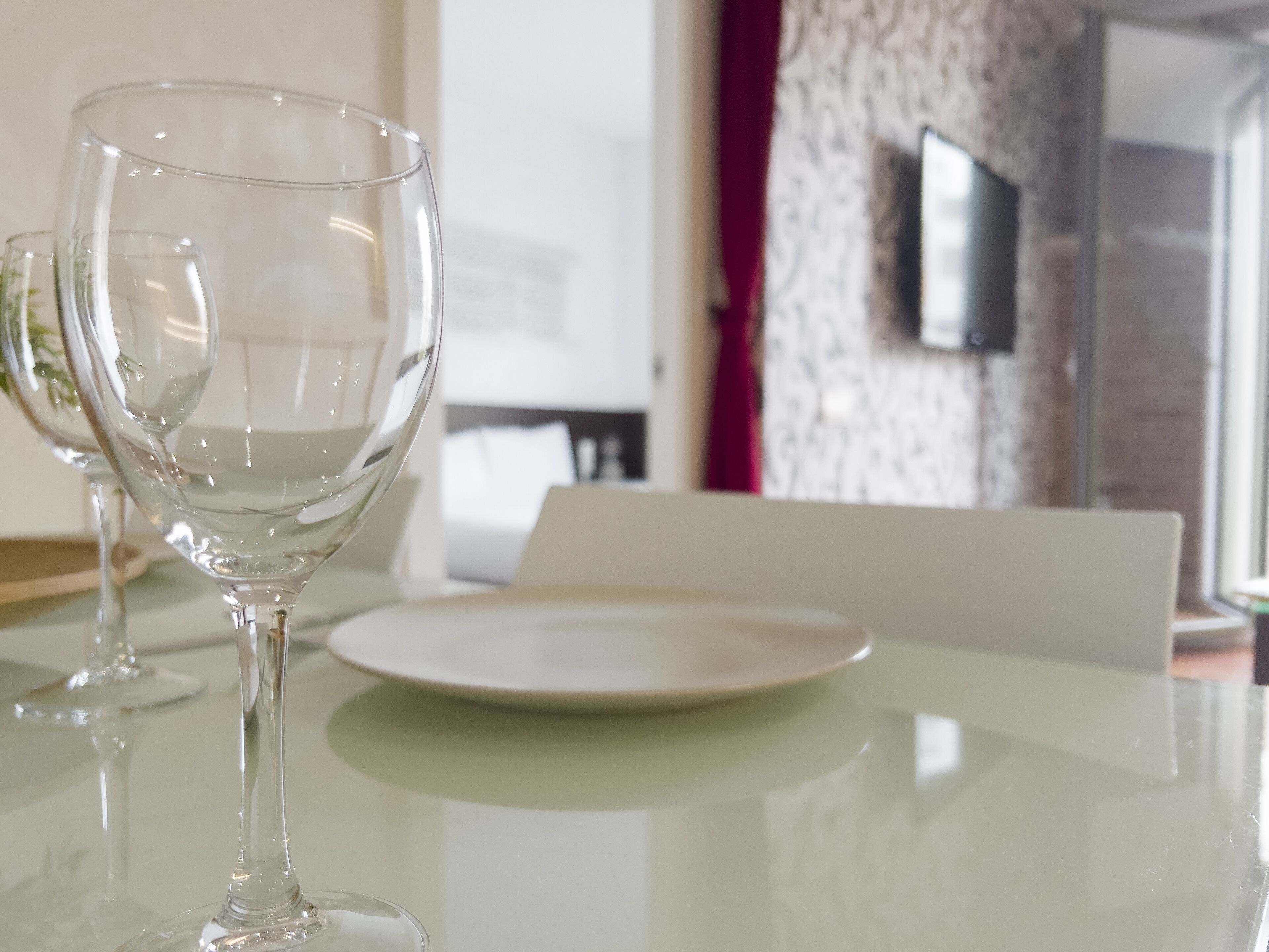 A glass table with two wine glasses and a white plate.
