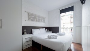 A modern hotel room with a large bed, a white brick wall, a wooden floor, and a balcony with a view. - Enjoybcn Gaudi Apartments (Barcelona)