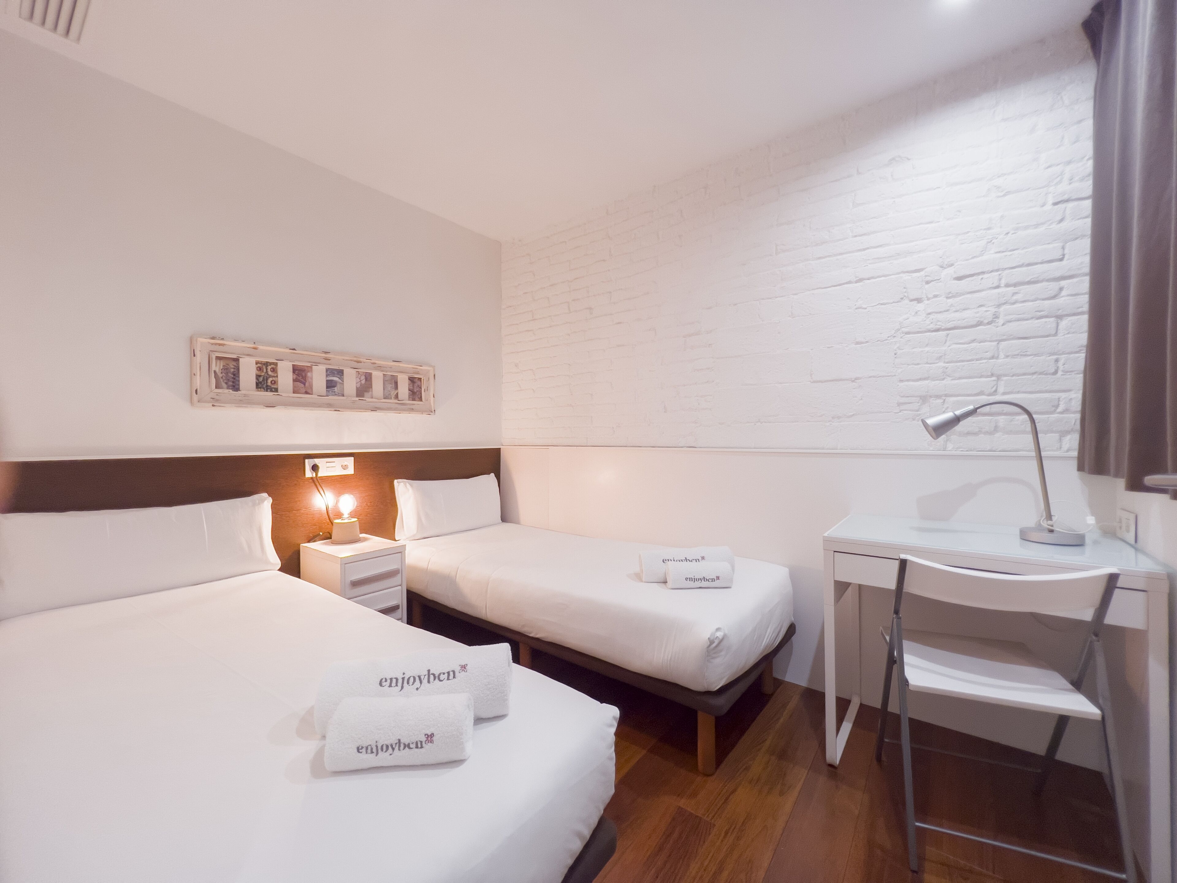 Habitación de hotel con dos camas, un escritorio y una silla. Hay toallas con el texto "enjoyben".