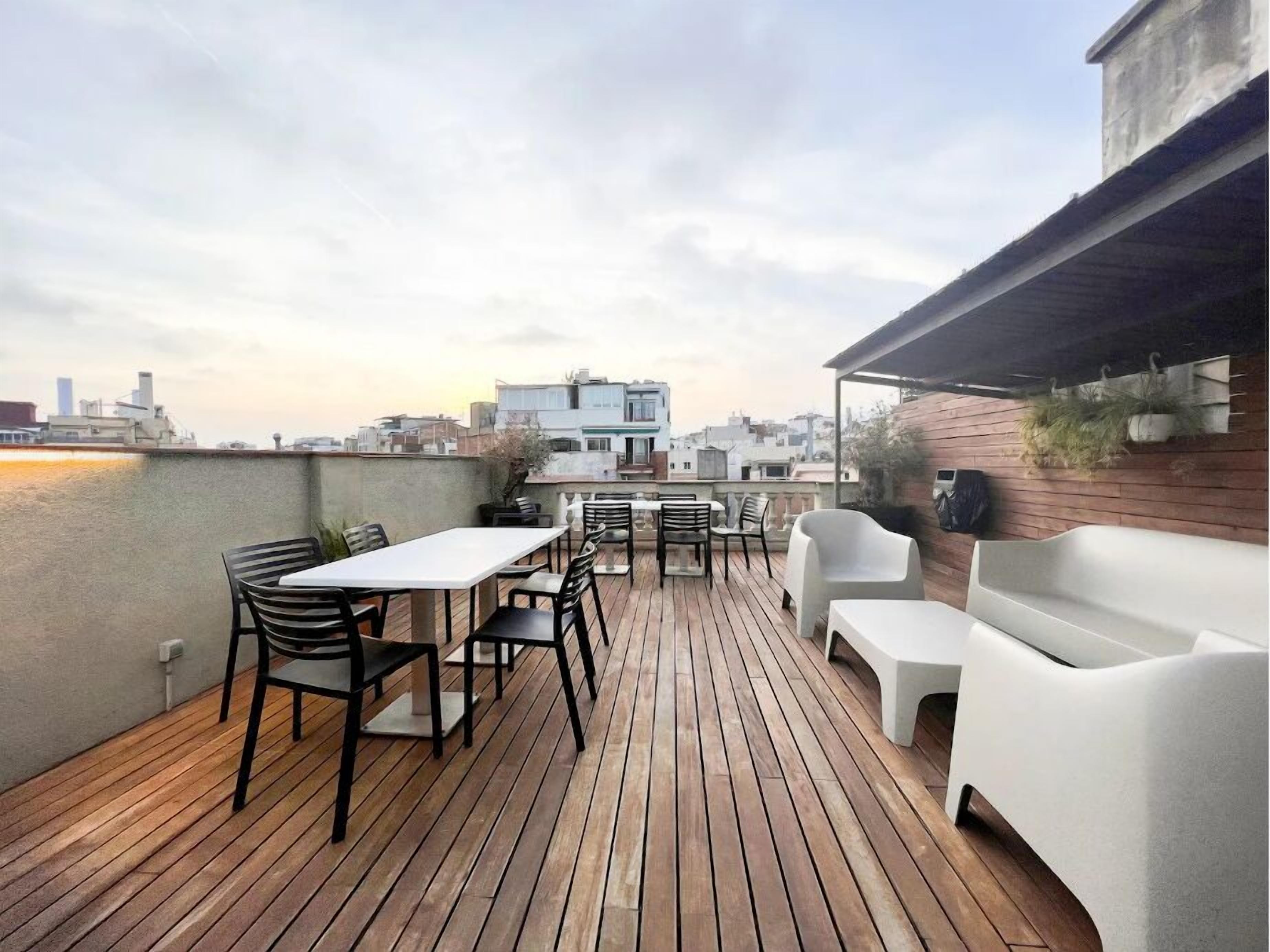Een dakterras met een houten terras, witte tuinmeubels en uitzicht op de stad.