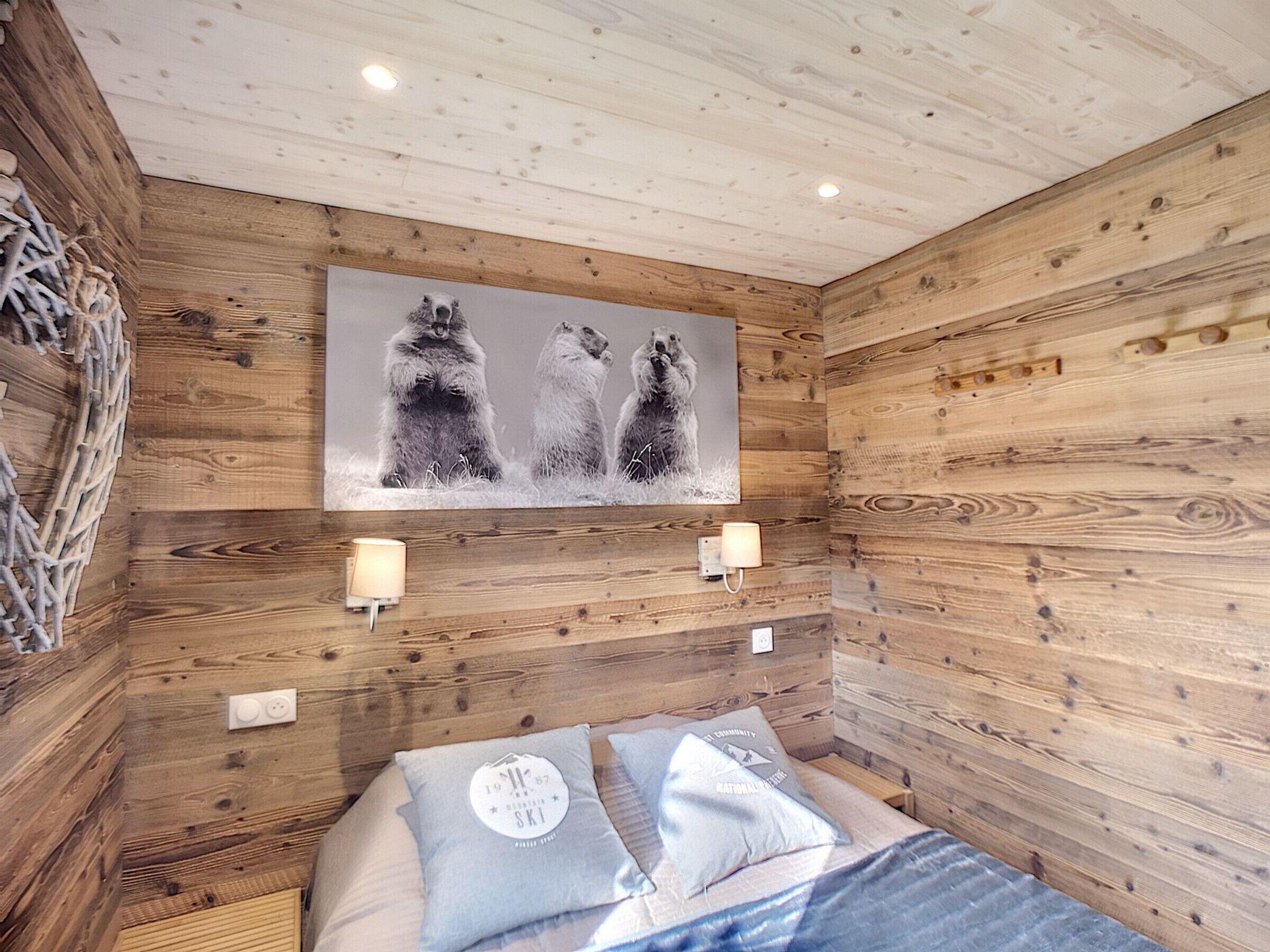 Una stanza in legno con un letto, due lampade a parete e un quadro con tre orsi.
