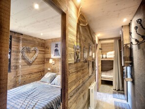 A wooden interior with a bed, a heart-shaped decoration, and a wall-mounted light fixture.