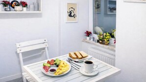 Une table de petit-déjeuner avec des toasts, des œufs et du café, placée devant un mur blanc orné d’une fenêtre et d’une étagère avec des objets décoratifs.