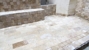 Une terrasse carrelée avec un mélange de carreaux beige et bruns, une petite marche menant à un niveau supérieur et un mur agrémenté d’un paravent.