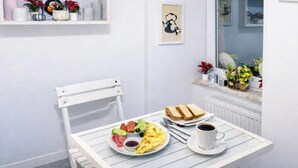 A breakfast table with toast, eggs, and coffee, set against a white wall with a window and a shelf with decorative items. - Istanberry - Paradise Apartments (Istanbul)