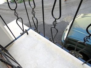 Une porte en métal avec un portail blanc, un sol en béton et une voiture bleue garée à l’extérieur.