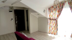 A room with a red sofa, a wooden floor, a ceiling fan, and a colorful curtain. - Istanberry - Paradise Apartments (Istanbul)