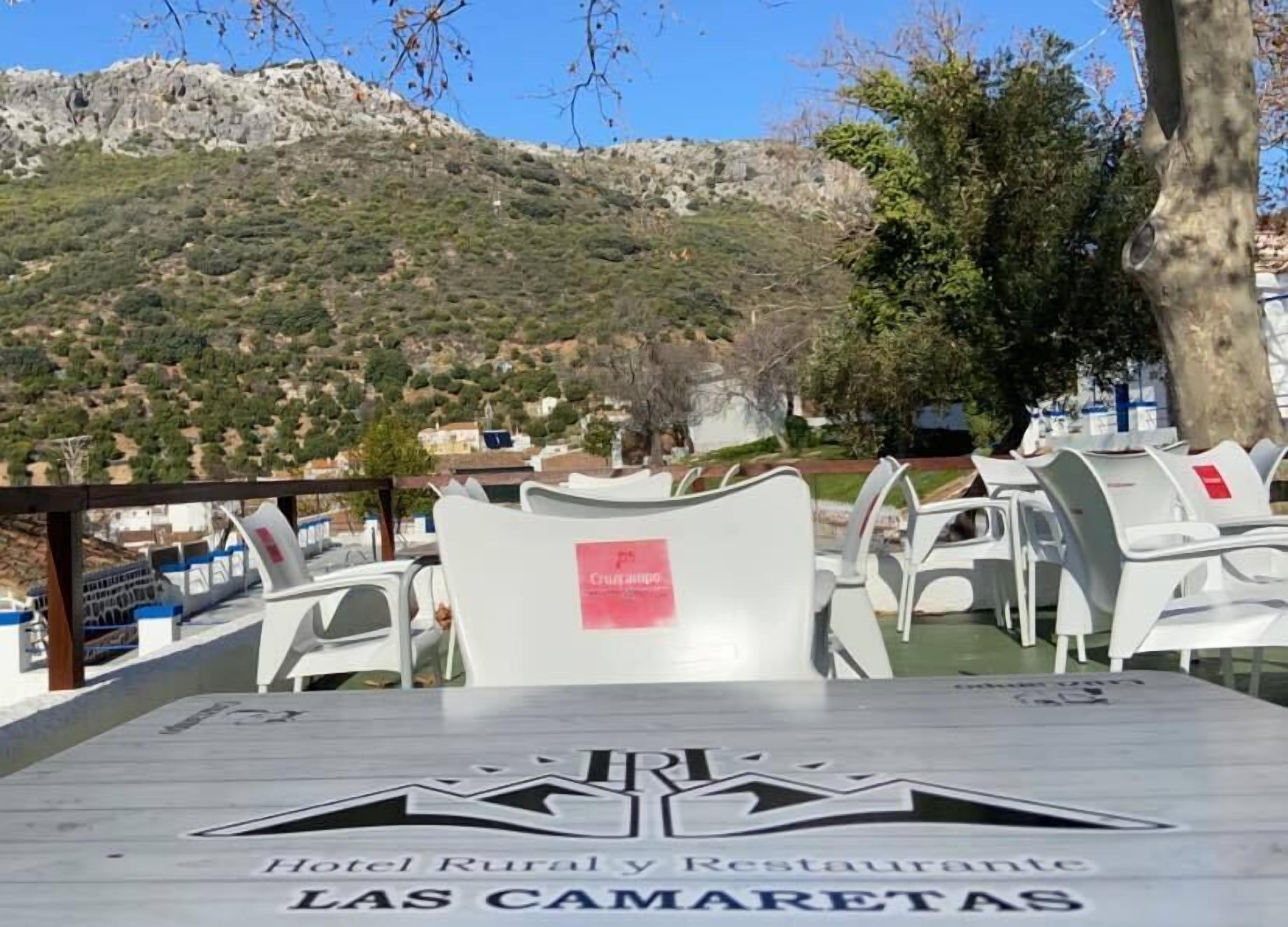 Terraza de restaurante con sillas de plástico blanco y una mesa con el logotipo "Hotel Rural y Restaurante LAS CAMARETAS".