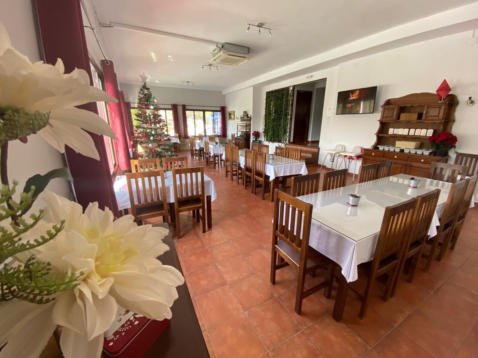 A dining area with multiple tables and chairs, a Christmas tree, and a television on the wall.