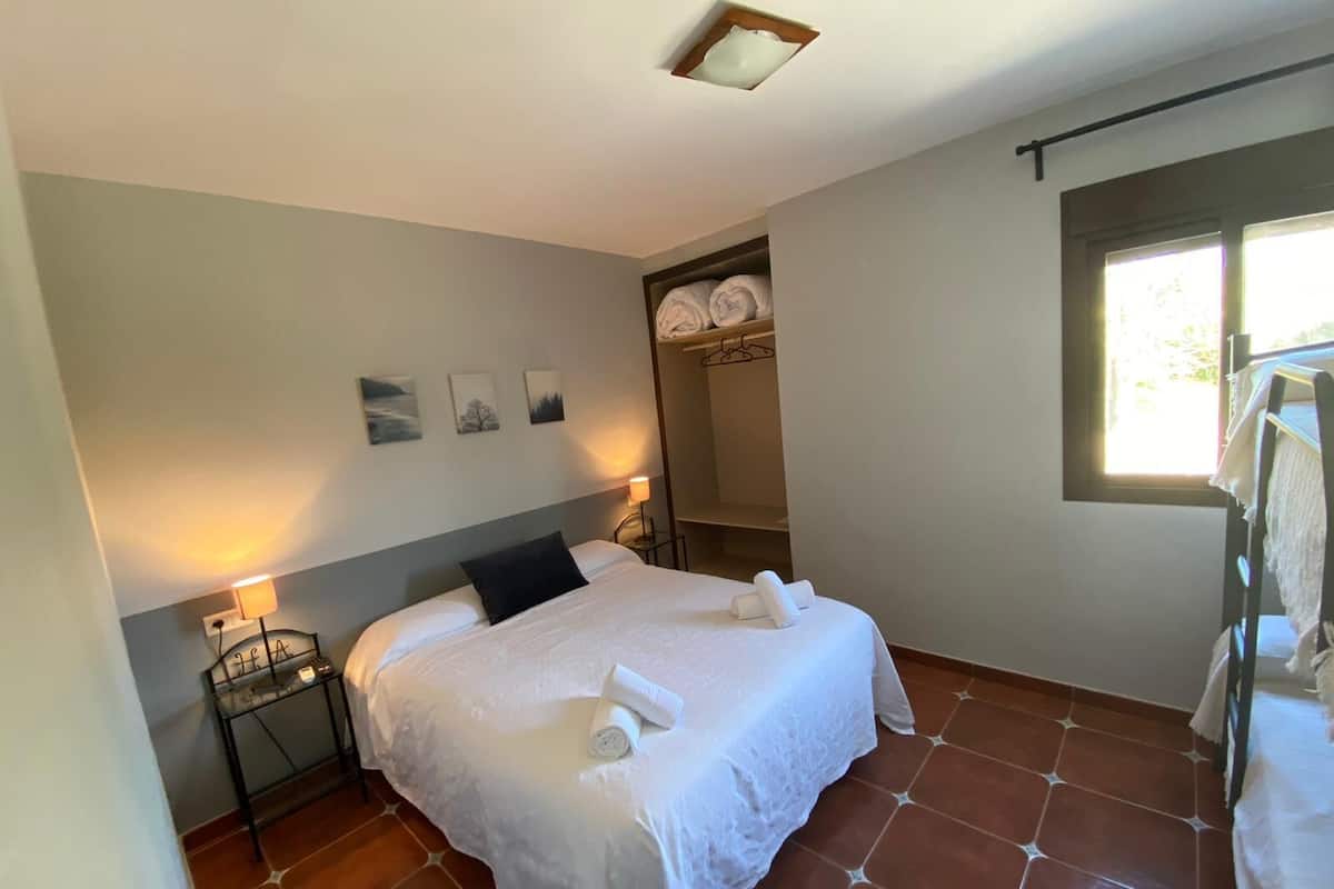 Une chambre à coucher comprenant un lit, une table de chevet, une commode, une fenêtre et un placard avec des vêtements suspendus.