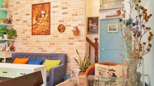 Ein Wohnzimmer mit Backsteinwand, einer Couch mit bunten Kissen, einem Couchtisch und einer Tür mit der Aufschrift 'Lille'.