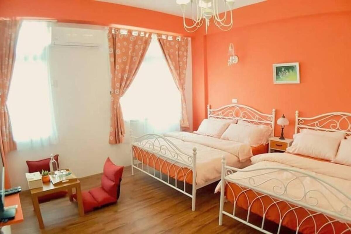 A room with two beds, a small table, a chair, and a window with curtains.