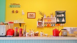 Un coin cuisine avec un mur jaune, une étagère contenant des ustensiles de cuisine, un mixeur et une machine à café.