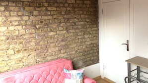 A room with a brick wall, a pink sofa, a small table, and a door with colorful panels. - Istanberry - Dream Apartments (Istanbul)