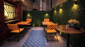 An outdoor seating area with tables and chairs, a blue patterned rug, and a green wall with plants. - Istanberry - Dream Apartments (Istanbul)
