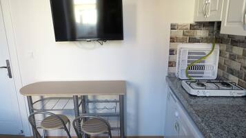 Cocina compacta con un televisor en la pared, una pequeña mesa de comedor con dos sillas y una estufa a gas.