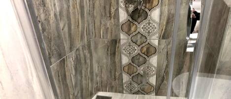 A shower area with a marble wall and a decorative panel.
