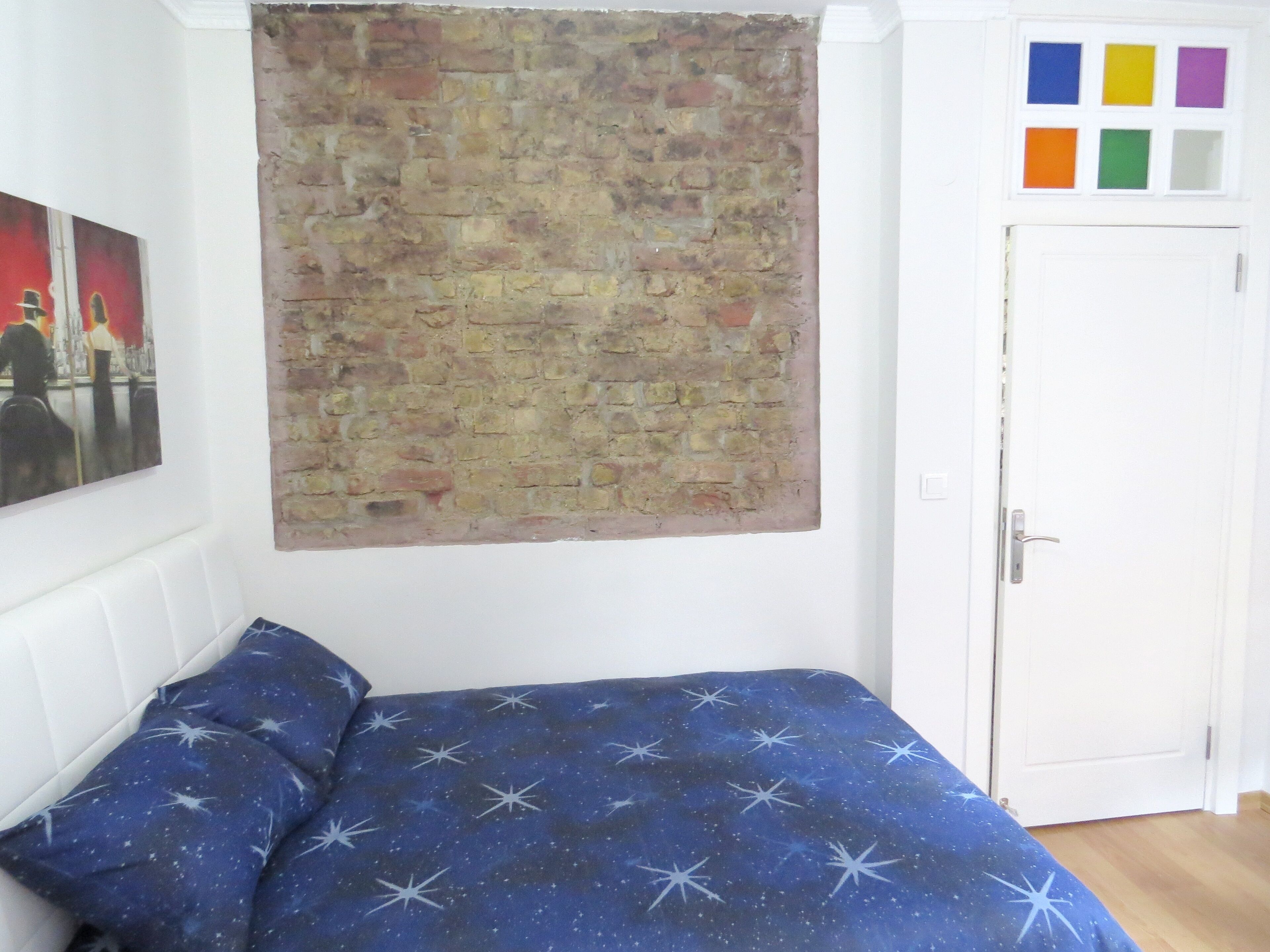 A bedroom with a brick-patterned wall hanging, a bed with a starry blue bedspread, and a door with colorful square stickers.