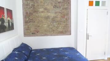 A bedroom with a brick-patterned wall hanging, a bed with a starry blue bedspread, and a door with colorful square stickers.