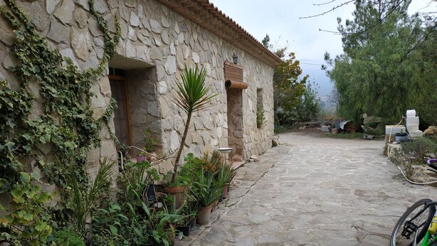 A stone building with a stone-paved courtyard, potted plants, and a bicycle. - Casa Guarrios, well tailor. Number 7 (Moratalla)