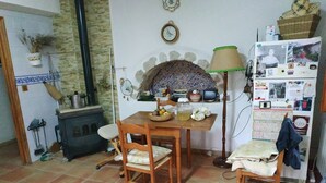 A cozy kitchen with a tiled floor, wooden chairs, a table with a basket of fruit, a stove, and a refrigerator covered with magnets and photos. - Casa Guarrios, well tailor. Number 7 (Moratalla)