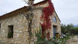 A rustic stone building with a tiled roof, a small arched window, and a door. - Casa Guarrios, well tailor. Number 7 (Moratalla)
