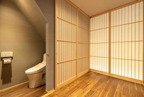 A bathroom with a toilet, wooden flooring, and a shoji screen door.