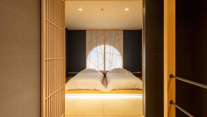 Une pièce de style japonais traditionnel, avec un sol recouvert de tatamis, un lit bas avec une literie blanche et une porte coulissante en papier de riz (shoji).