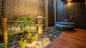 Un espace de détente en bois agrémenté d’une lanterne en pierre, d’une plante de bambou et d’un bassin en pierre.