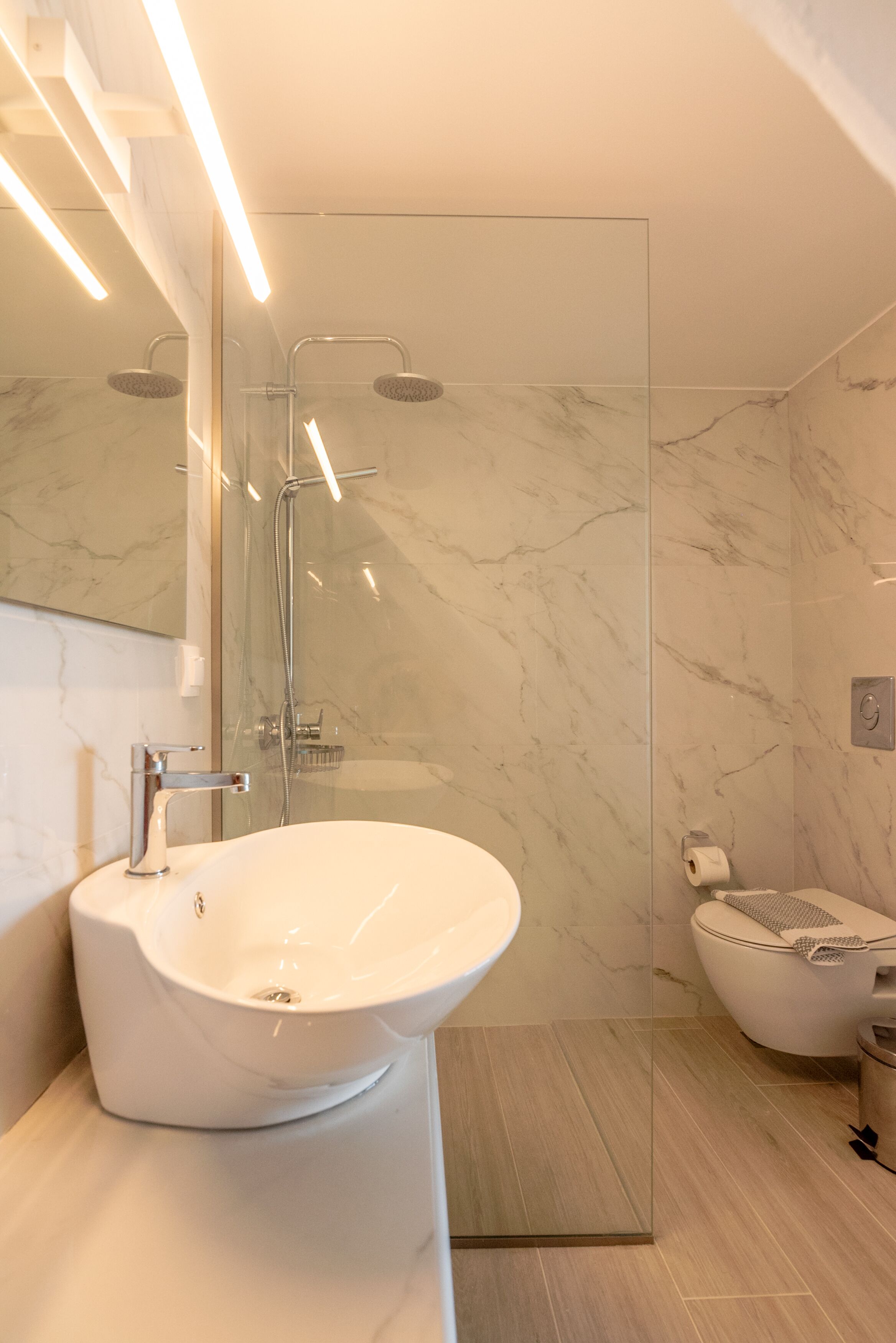 A modern bathroom with a large white sink, a glass-enclosed shower, and a toilet.