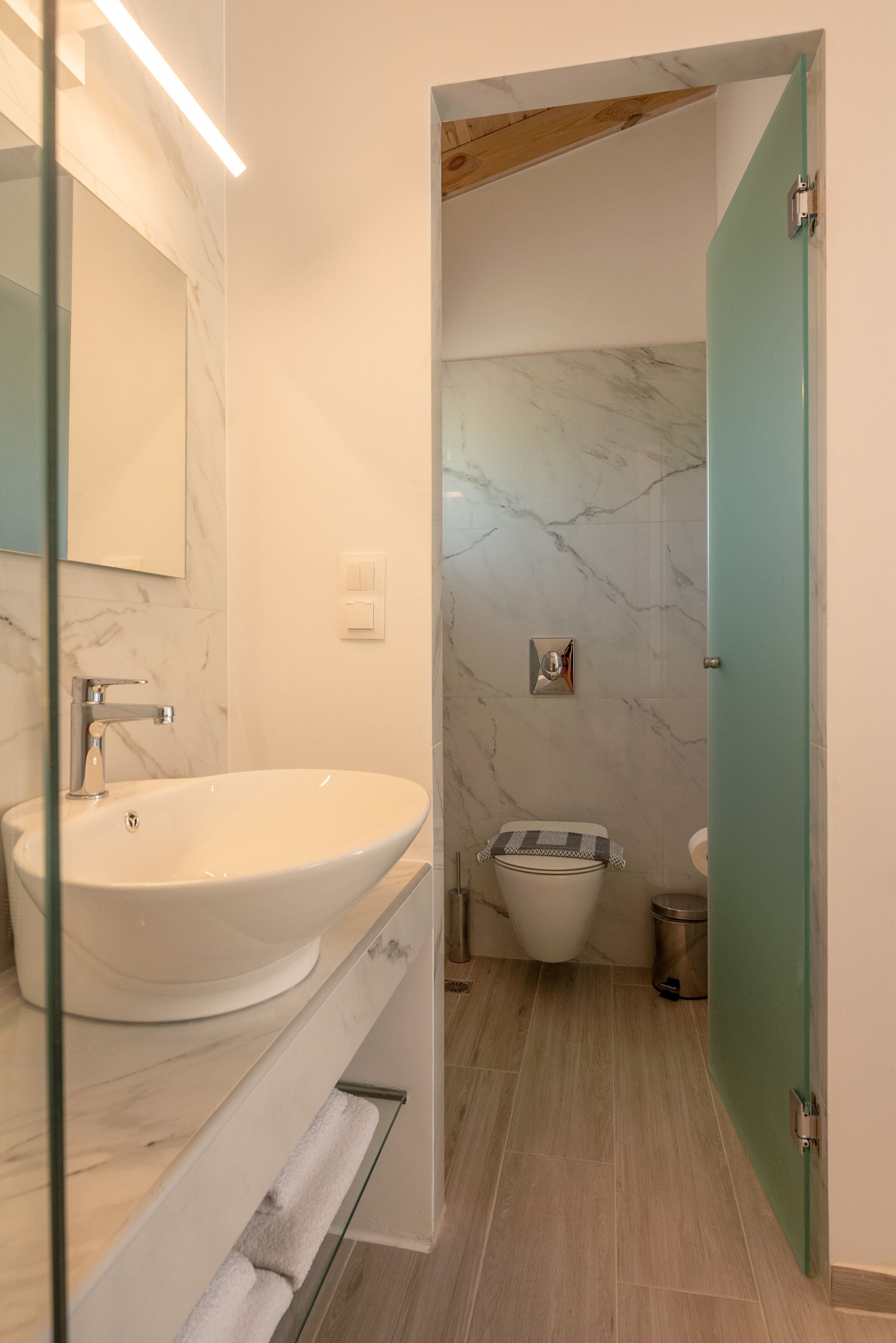 A modern bathroom with a large white sink, a mirror, and a marble wall.