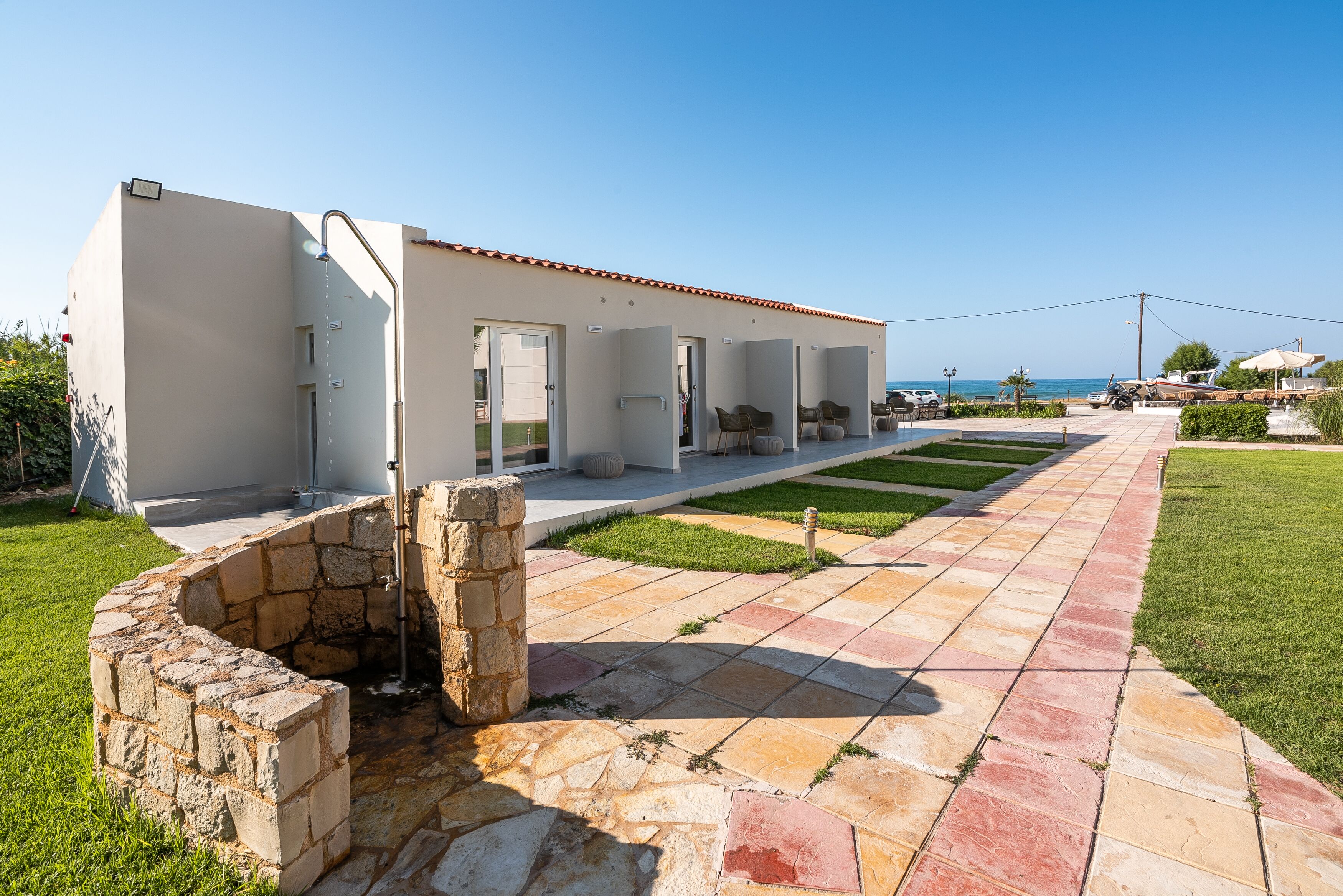 A modern building with a stone wall entrance, a paved patio, and a view of the sea.