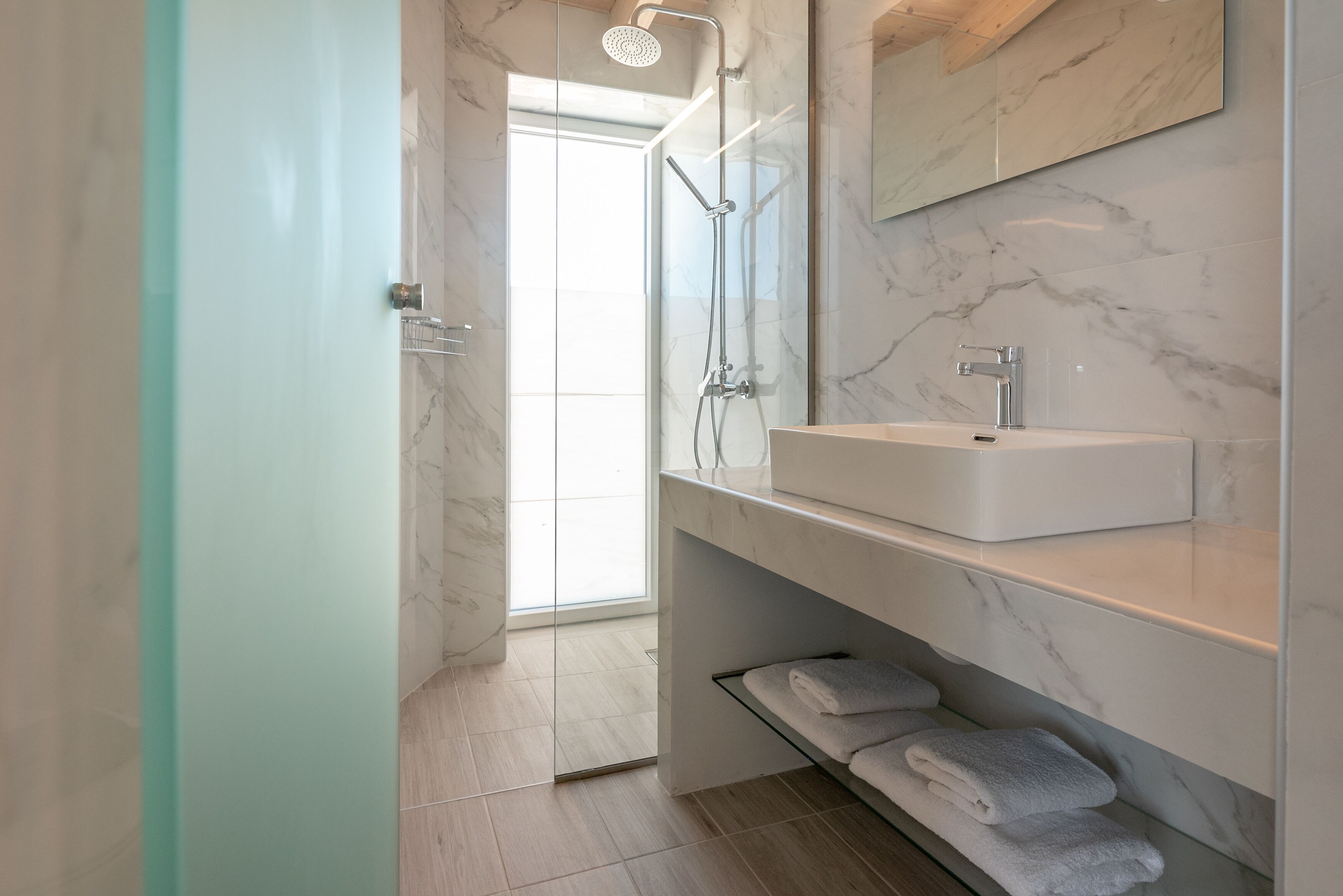 A modern bathroom with a glass shower enclosure, a white sink, and a marble backsplash.