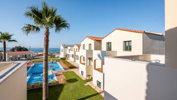 Un área de piscina con palmeras, cielo despejado y vista al mar.