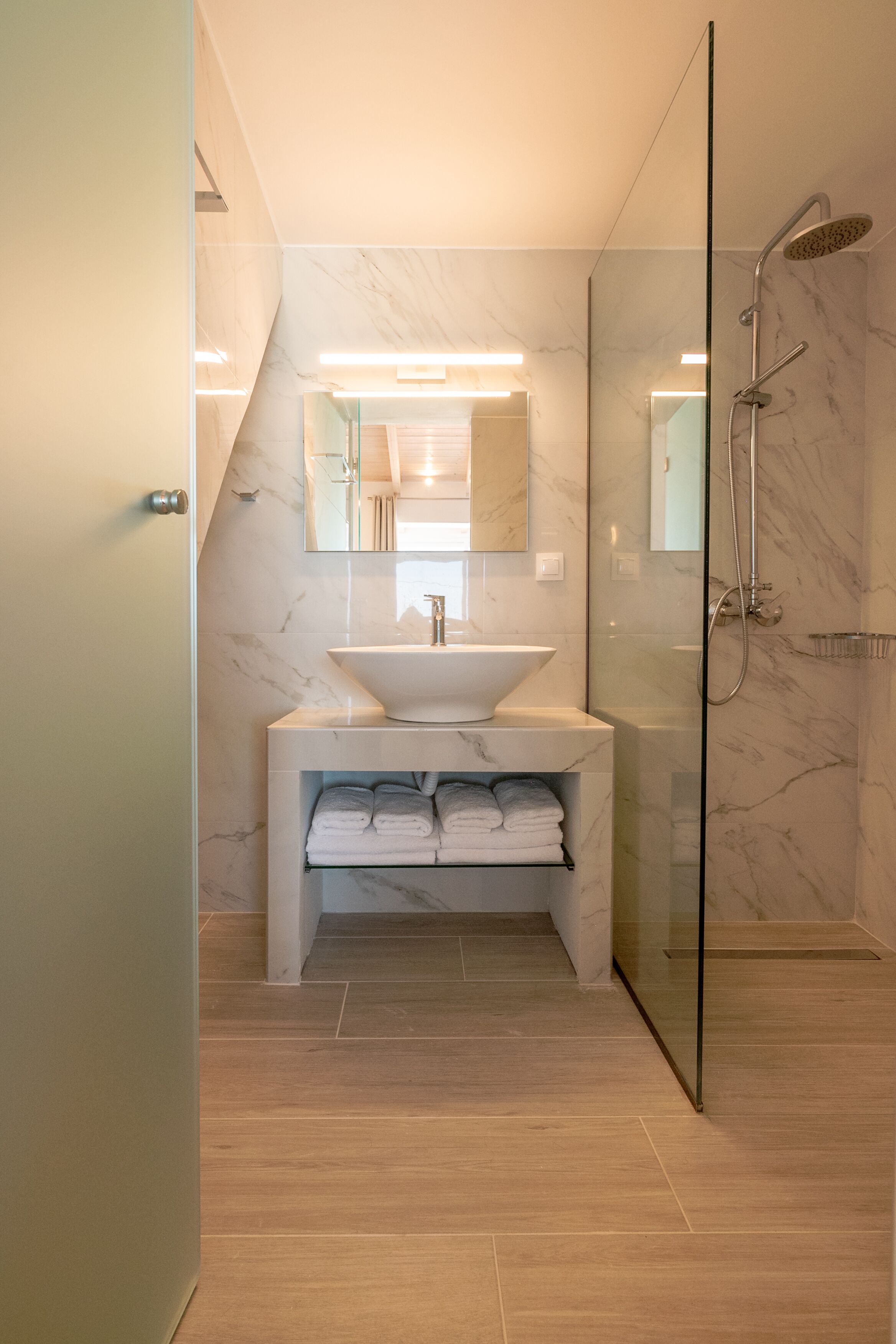 A modern bathroom with a glass-enclosed shower, a marble sink, and a built-in towel rack.