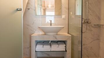 A modern bathroom with a glass-enclosed shower, a marble sink, and a built-in towel rack.