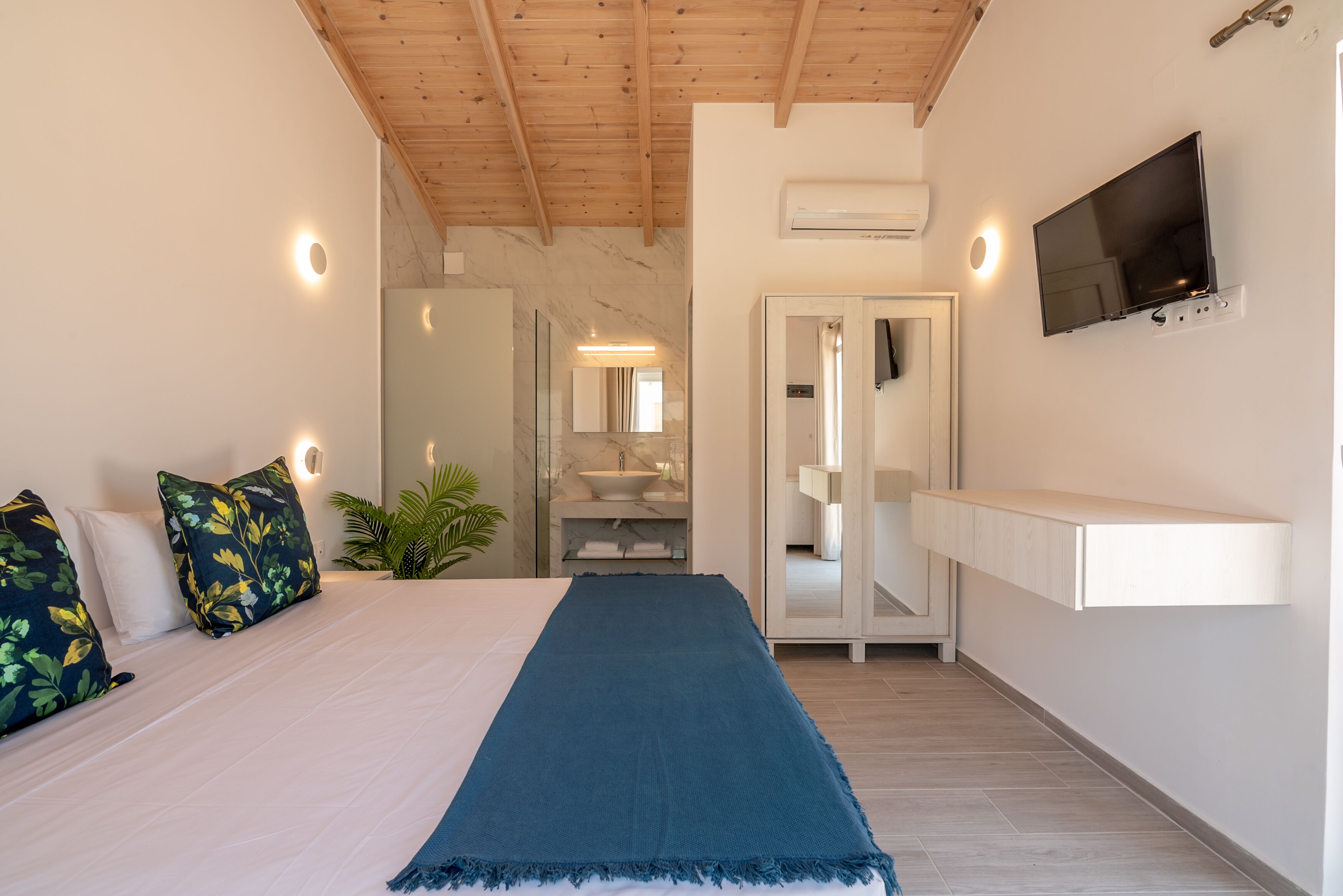 A bedroom with a bed, a TV, a mirror, and a bathroom visible through an open door.