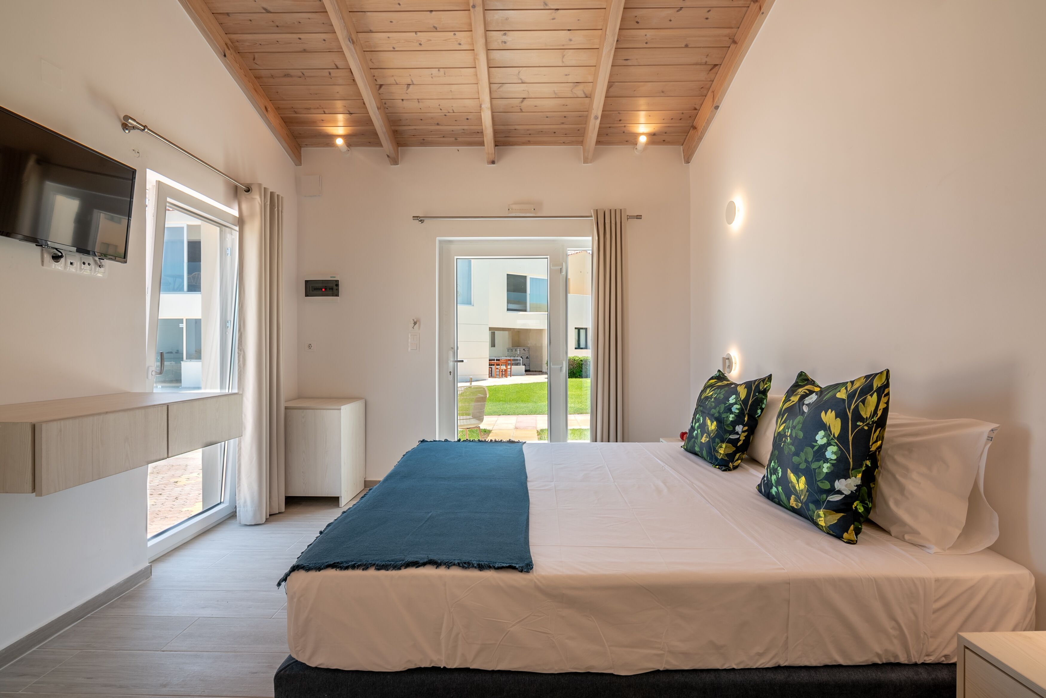 A bedroom with a bed, a TV mounted on the wall, and a window with curtains.