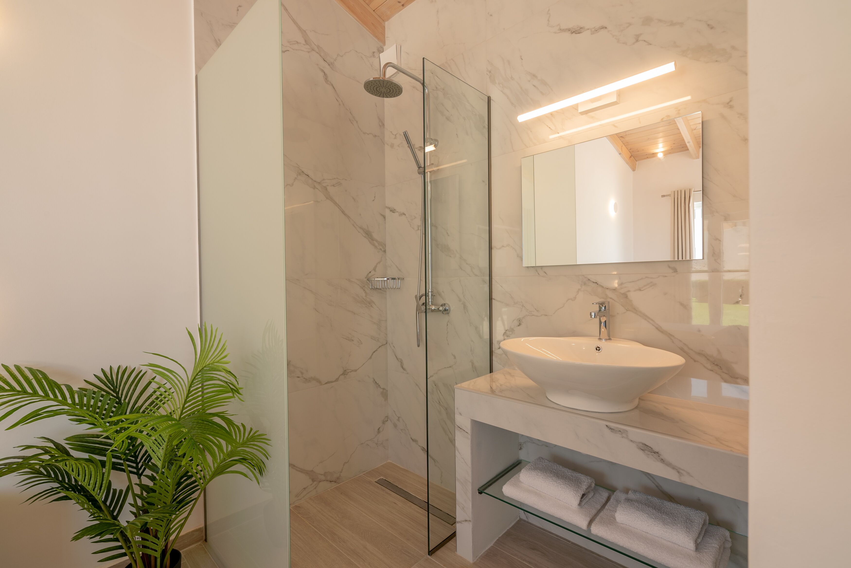 A modern bathroom with a glass-enclosed shower, a white sink, and a large mirror.