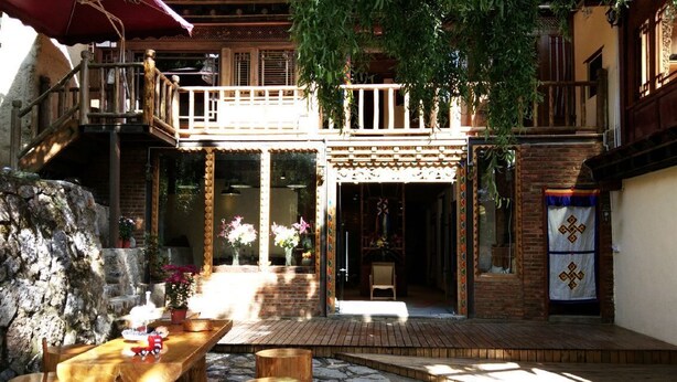 Un patio con una mesa de madera y bancos, un muro de piedra y un balcón con barandilla.