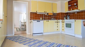 Cozinha com armários amarelos, lava-louças branca e fogão. Um tapete estampado cobre o chão.