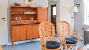 Quarto com um armário de madeira, duas cadeiras de vime com almofadas, um quadro na parede e uma porta que dá para outro cômodo.