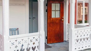 Uma porta de madeira com painel de vidro, um alpendre branco com grades decorativas e uma pequena caixa de correio azul.