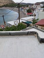 A coastal town with buildings overlooking the beach, a clear view of the sea, and a paved area in the foreground.