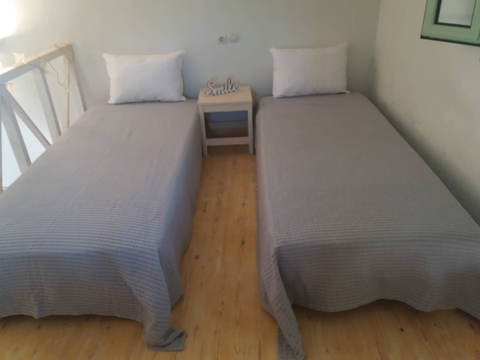 A twin room with two single beds, a nightstand, and a small table with a 'Smile' sign.